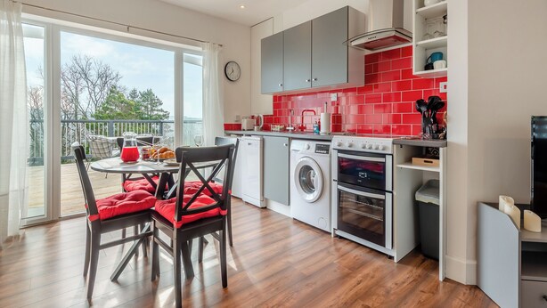 Eine moderne Küche mit roter Rückwand, einer Waschmaschine, einem Backofen und einem Essbereich mit Tisch und Stühlen.