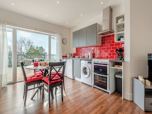 A modern kitchen with a red backsplash, a washing machine, an oven, and a dining area with a table and chairs. - 2 bedroom accommodation in Goodwick (Goodwick)