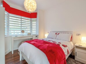 Une chambre à coucher avec un lit, des tables de chevet, un bureau et une fenêtre avec des stores.