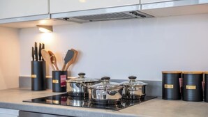 Eine moderne Küche mit Edelstahlkochgeschirr auf einer Induktionskochplatte, einem Utensilienhalter und schwarzen Vorratsbehältern auf der Arbeitsfläche.