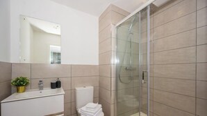 Ein modernes Badezimmer mit Duschkabine aus Glas, einem weißen Waschbecken mit Pflanze in Goldtöpfen und einer Toilette.