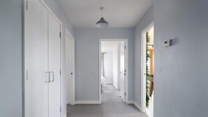 A hallway with white doors, a ceiling light, and a view into another room.