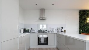 A modern kitchen with white cabinetry, a stainless steel range hood, and a built-in oven.