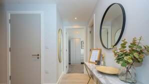 A hallway with a door, a mirror, a vase with flowers, and a framed menu on a counter. - Modern, Spotless & Close to City Hotspots! (Greater Manchester)
