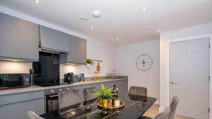 A modern kitchen with grey cabinets, a black countertop, and a dining table with chairs. - Modern, Spotless & Close to City Hotspots! (Greater Manchester)