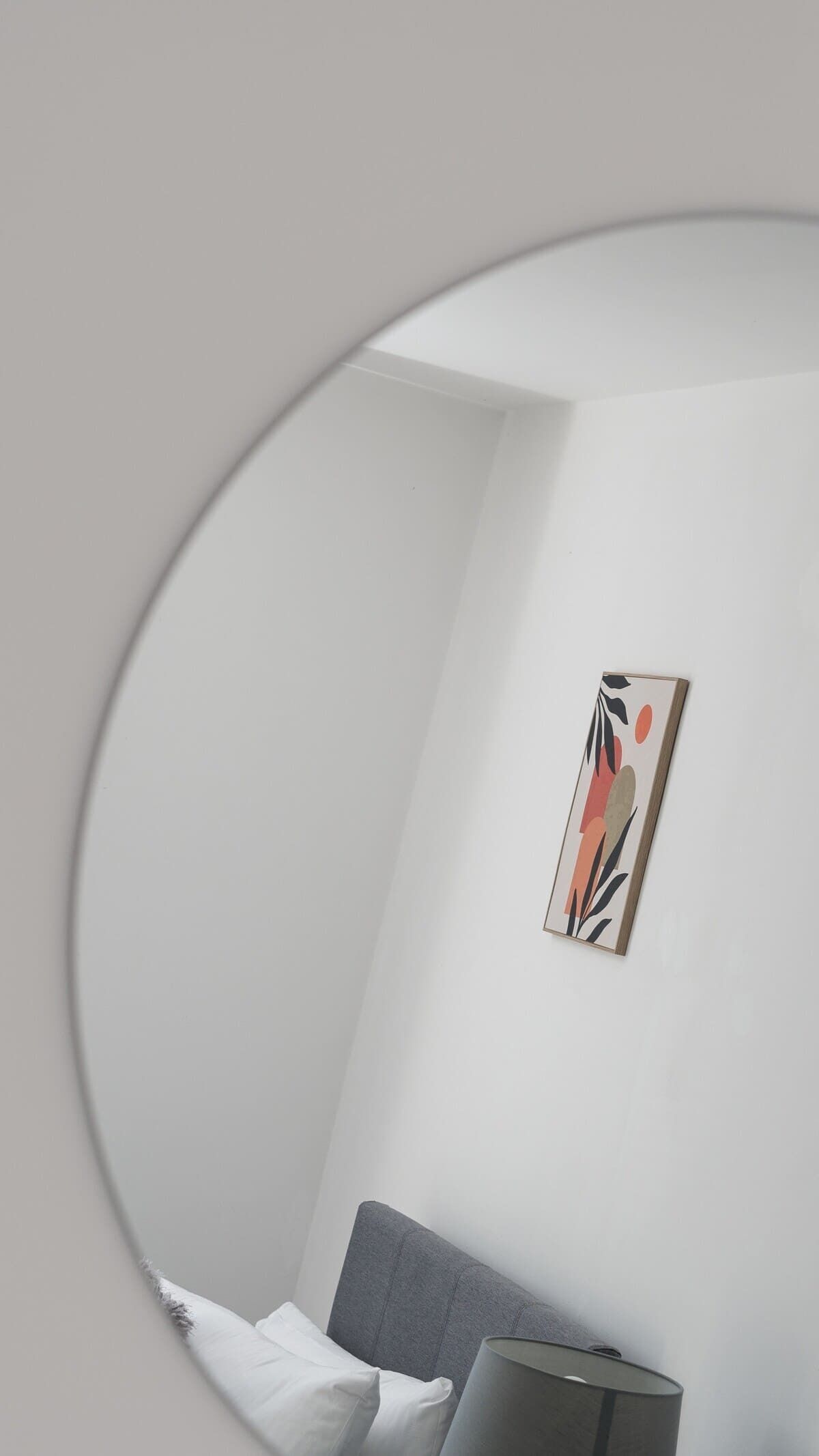 A minimalist bedroom with a bed, a gray headboard, a bedside lamp, and a wall-mounted abstract painting.