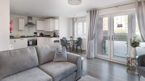 A modern apartment with a grey sofa, dining area, kitchen, and large sliding glass doors to a balcony. - Spacious 2-Bedroom Home with Parking & Wi-Fi (Milton Keynes)