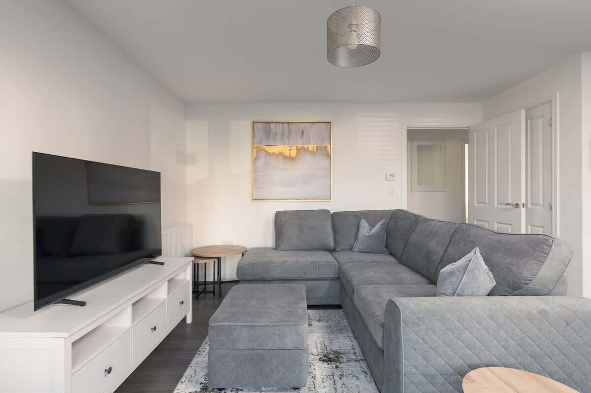 Una sala de estar moderna con un sofá seccional gris, un televisor de pantalla plana, una mesa de centro y una alfombra.