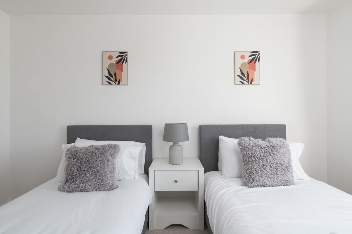 A minimalist hotel room with two beds, a nightstand, and two wall-mounted artworks.