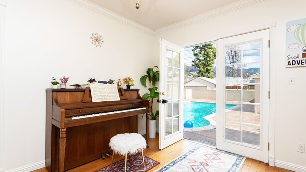 Ett piano med noter, en vit dörr som leder till en pool och en dekorativ matta.