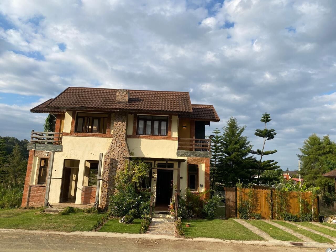 A two-story house with a stone facade, a balcony on the upper floor, and a front entrance with a small porch.