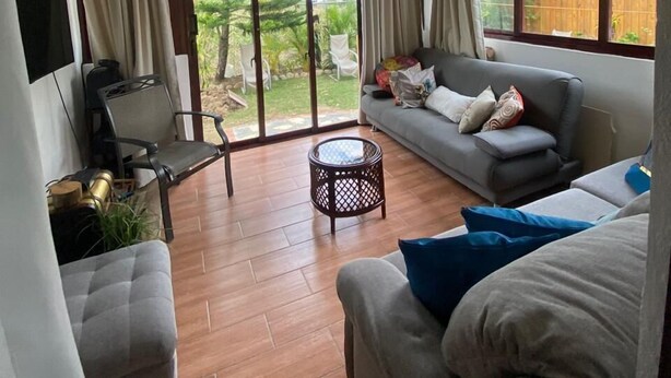 A spacious living room with a ceiling fan, a grey sofa, a coffee table, and a TV mounted on the wall.
