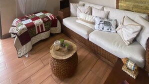 A living room with a white sofa, a wicker side table, a decorative wall piece, and a hanging light fixture.