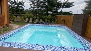 A rectangular swimming pool with blue mosaic tiles, surrounded by a wooden deck and a wooden fence.