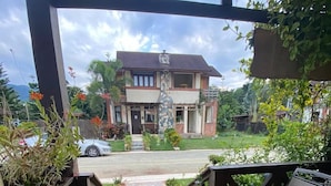 A covered patio area with a view of a house, potted plants, and a chair.