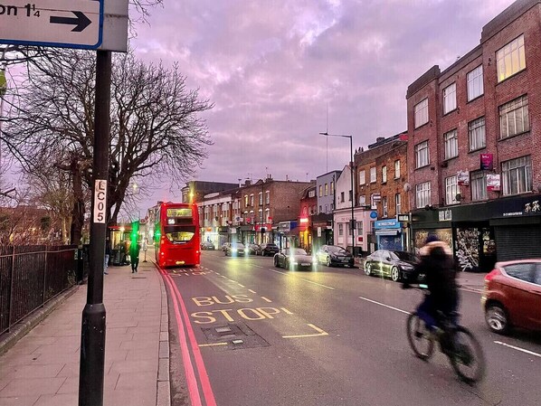 A street with a bus stop, buildings, and a cyclist. - Hackney Suites - Double En-suite Room (B1) (Greater London)