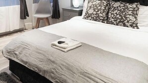 Un dormitorio con cama, dos sillas, una mesita de noche y una ventana con cortinas.
