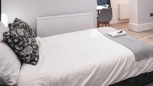 A modern bedroom with a bed, bedside table, and a desk with a chair. - Hackney Suites - Double En-suite Room (G2) (Greater London)