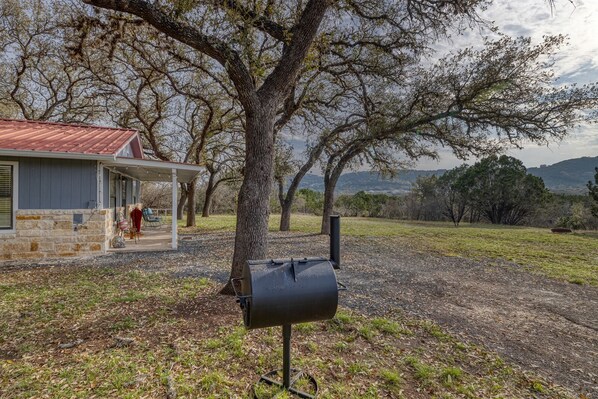 A house with a porch, a barbecue grill, and a view of trees and hills in the background.