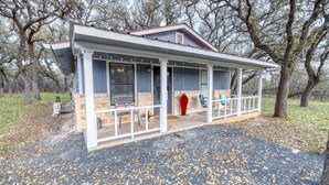 A covered porch with stone pillars, a red vase, and a bench. - Live Oak Cottage on a beautiful lot with large oak trees and fenced backyard. (Concan)