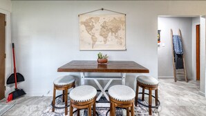 A dining area with a wooden table, four barstools, a world map on the wall, and a potted plant. - Live Oak Cottage on a beautiful lot with large oak trees and fenced backyard. (Concan)