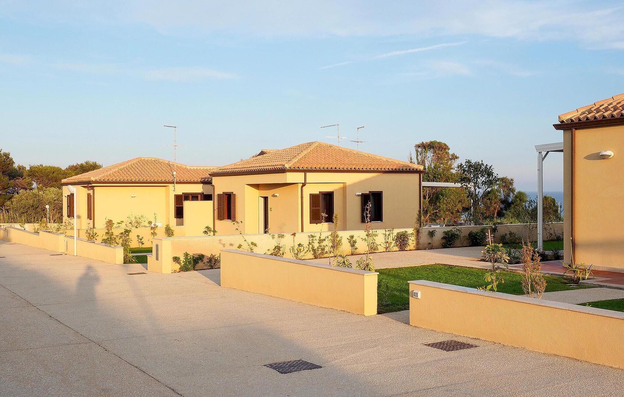 A row of two-story houses with tiled roofs, beige walls, and small front gardens.