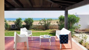 A covered outdoor seating area with two white chairs and a table, overlooking a beach and ocean.