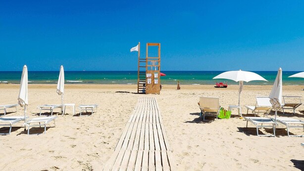 A beach with a wooden walkway leading to a lifeguard tower, white umbrellas, and beach chairs.