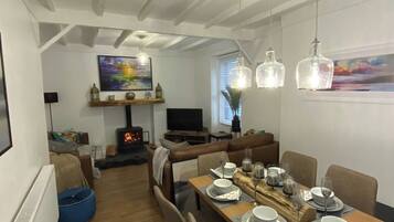 A dining area with a long table set for four, a fireplace, a television, and a painting on the wall.