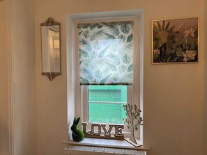 A window with a leaf-patterned blind, a decorative 'LOVE' sign, and a small plant.
