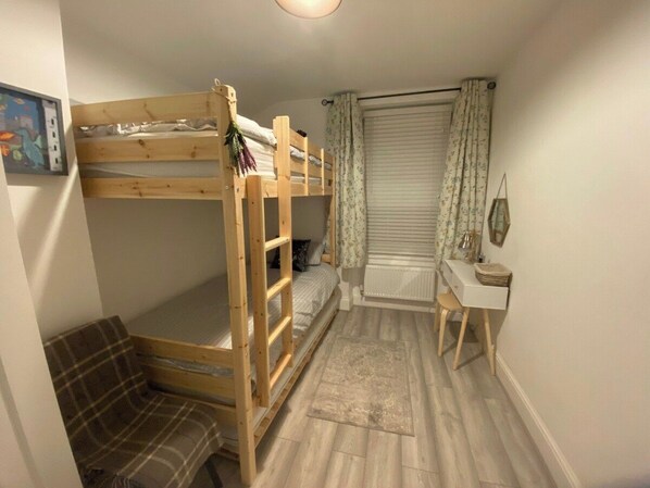 A bunk bed, a desk, a chair, a radiator, and a window with curtains.