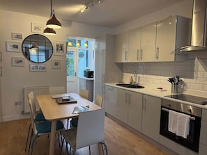 A modern kitchen with a dining area, featuring a table, chairs, a sink, and a stove. - Downtown cottage in heart of Medieval Conwy (Conwy)