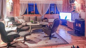 Un salon confortable avec un canapé, un fauteuil et une table basse. On y trouve également une télévision et une cheminée.