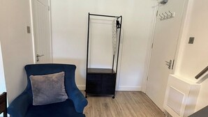 Et værelse med en blå lænestol, et sort metalstativ og et hvidt skab.