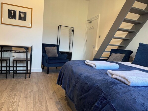 A bedroom with a bed, a chair, a desk, and a staircase.