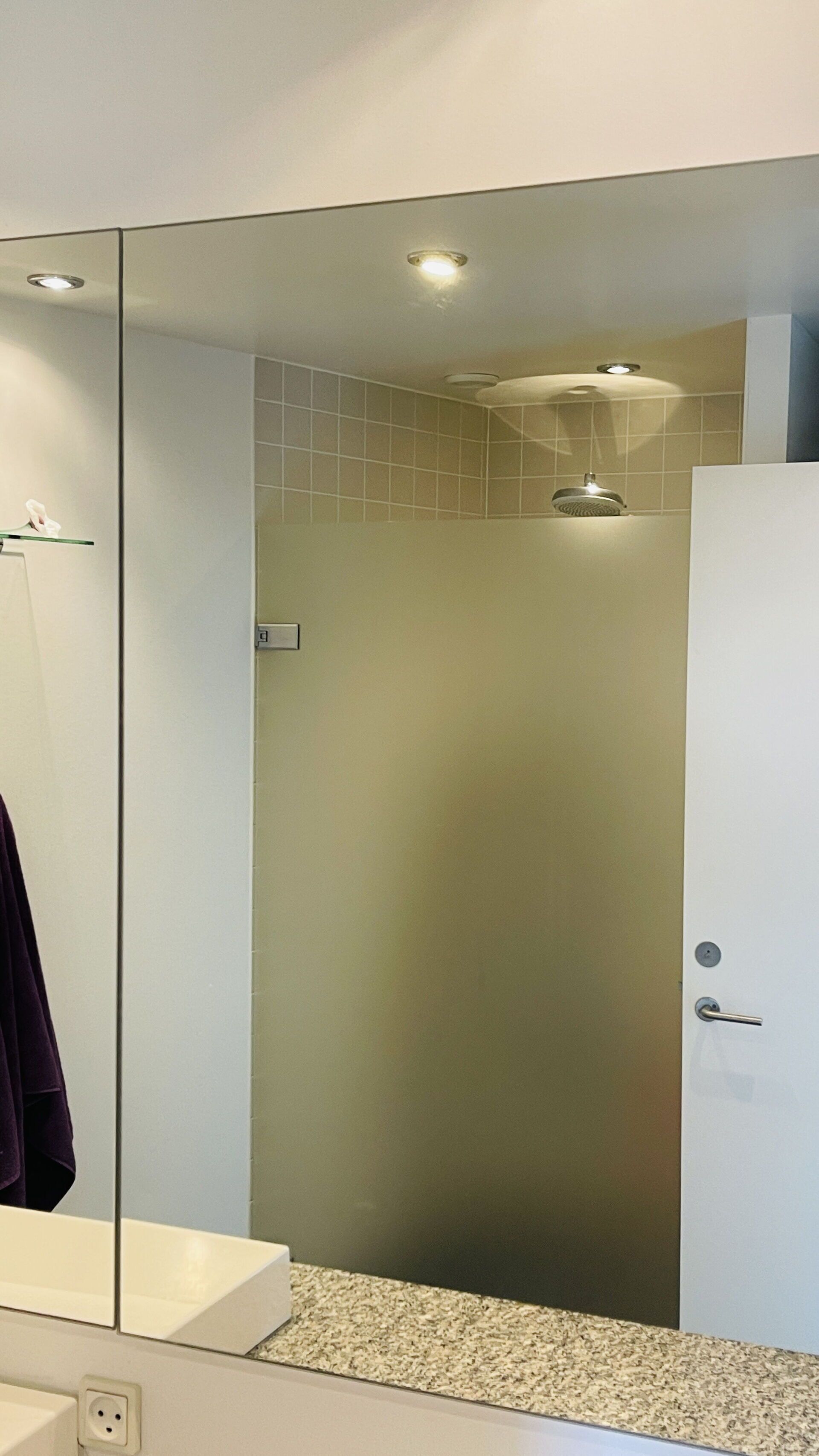 A bathroom with a glass shower enclosure, a white sink, and a mirror reflecting part of the room.