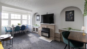 A modern living room with a fireplace, a flat-screen TV, and a dining area with chairs and a table. - Open Mind Property - Southsea with Free Parking (Portsmouth)