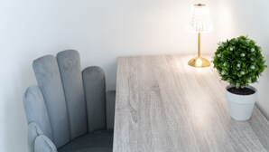 Eine Ecke des Raumes mit einem grauen Polsterarmlehnstuhl, einem Holztisch, einer Topfpflanze und einer Tischlampe.