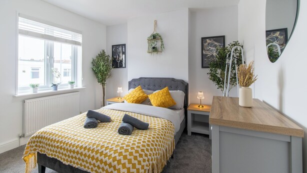 Ein Schlafzimmer mit einem Bett, Nachttischen, einem Fenster mit Jalousien und einem an der Wand befestigten Kunstwerk.