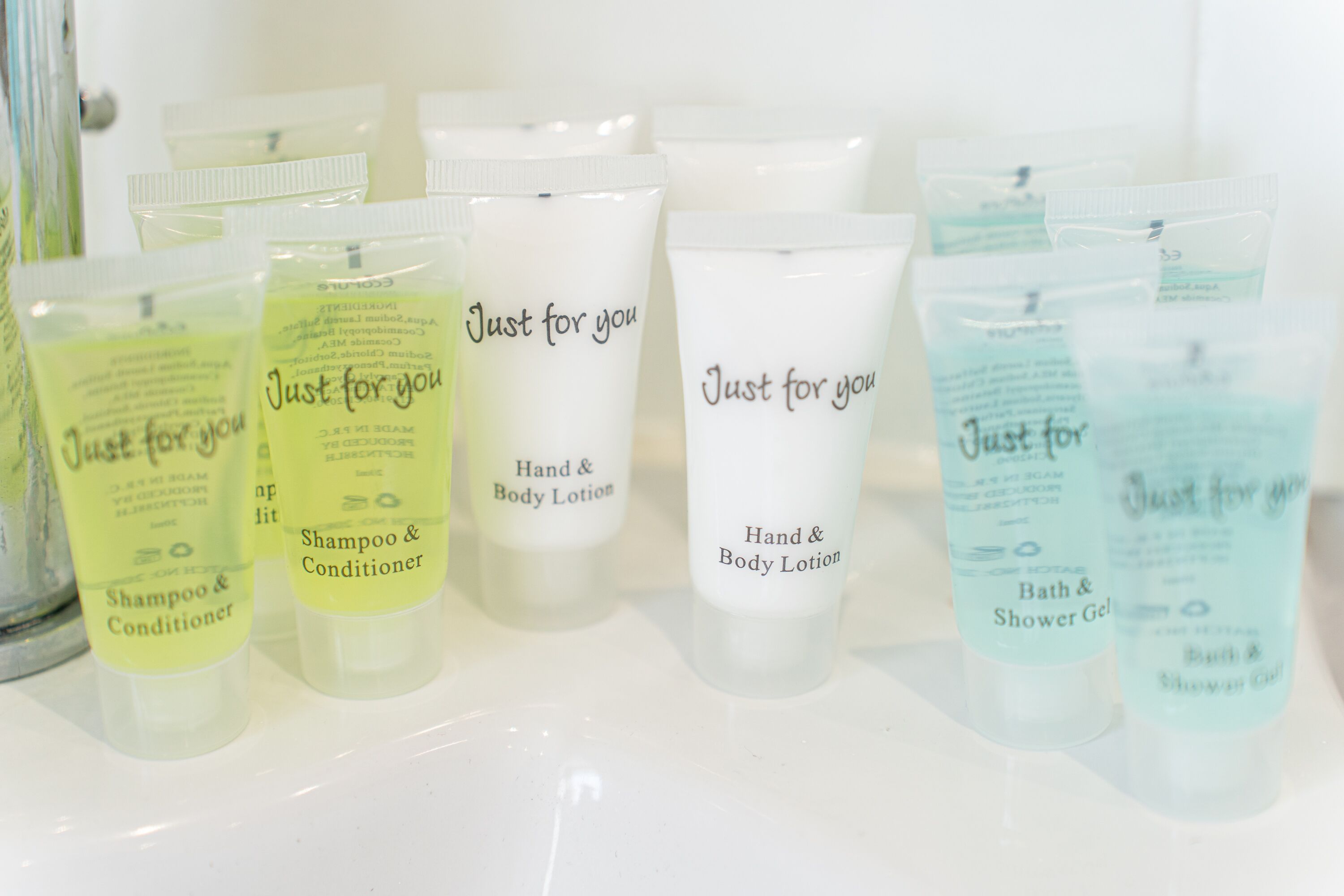 Verschiedene Pflegeprodukte wie Shampoo, Conditioner, Körperlotion und Duschgel, auf einer weißen Fläche angeordnet.