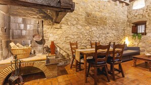 A rustic stone-walled room with a wooden table and chairs, a fireplace, and a stone bench. - Bravissimo Girona 1593, Medieval charm in the heart of Girona Jewish quarter (Girona)