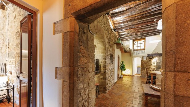 A stone-walled corridor with a tiled floor, leading to a dining area with a table and chairs. - Bravissimo Girona 1593, Medieval charm in the heart of Girona Jewish quarter (Girona)