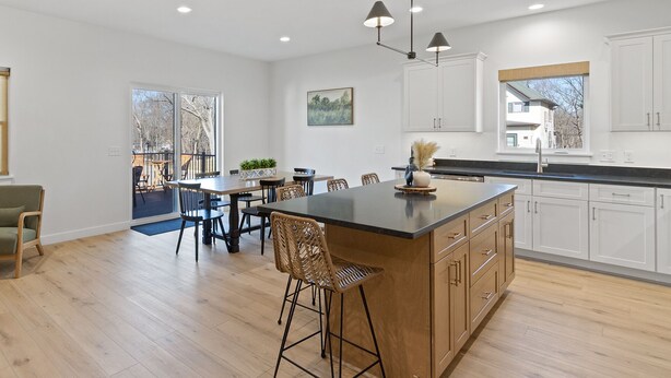 Une cuisine moderne dotée d’un îlot central, de meubles blancs et d’un coin repas offrant une vue sur l’extérieur.