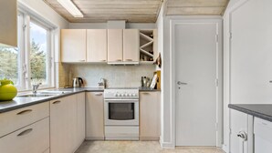 Eine kompakte Küche mit hellen Schränken, einem eingebauten Backofen und einem Fenster, das für natürliches Licht sorgt.