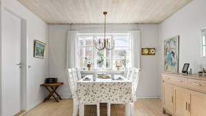 Ein Esszimmer mit Tisch für vier Personen, einer Chandelüster und Blick durch große Fenster.