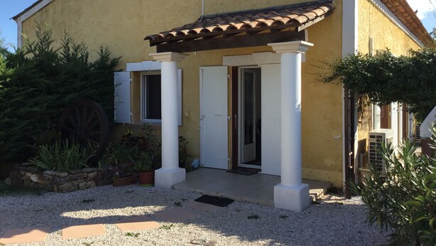 Um edifício amarelo com telhado de cerâmica, varanda com colunas brancas e uma porta.