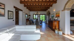 A spacious living area with a white leather sofa, wooden ceiling beams, and a fireplace.