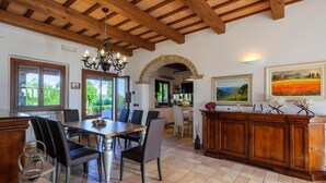A spacious dining area with a wooden table and chairs, a chandelier, and a view of the outdoors through large windows.