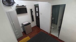 A small, compact room with a wardrobe, a small fridge, a TV, and a bathroom with a glass door. - Casita Libertad Barranco (Lima)