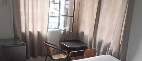 A hotel room with a bed, a desk, a chair, a TV, and a window with curtains.